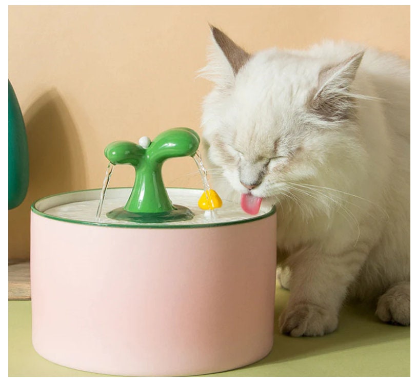 a white cat drinking water from a green faucet