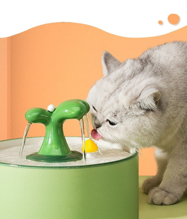 a cat drinking water from a green faucet